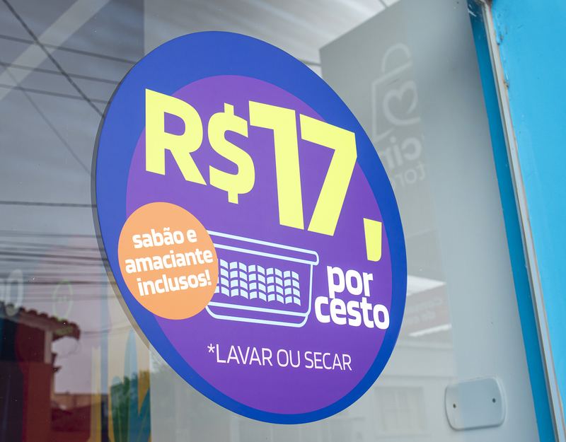 Adesivo na vitrine da Lavô anunciando R$ 17 por cesto, com sabão e amaciante inclusos, para lavar ou secar